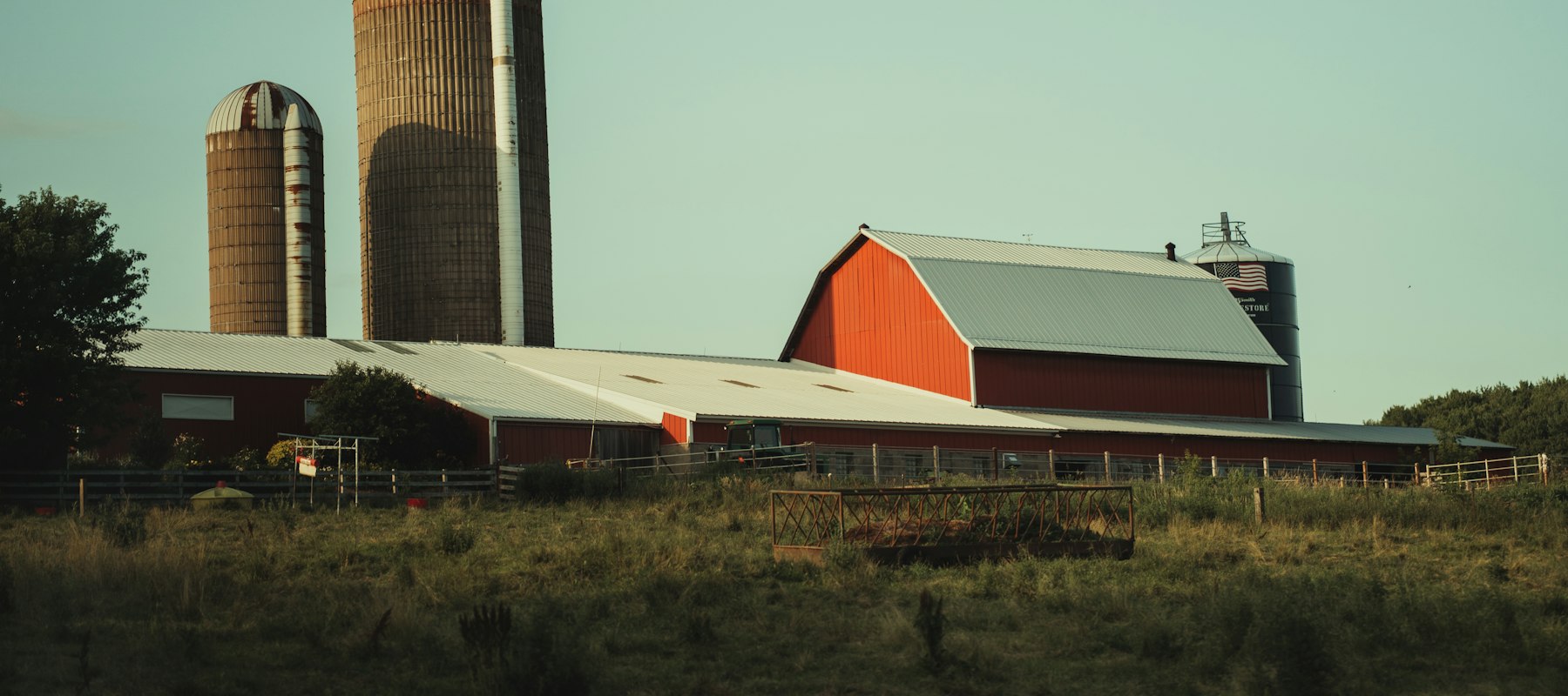 A working dairy farm with a red barn and tall silos at the edge of a field